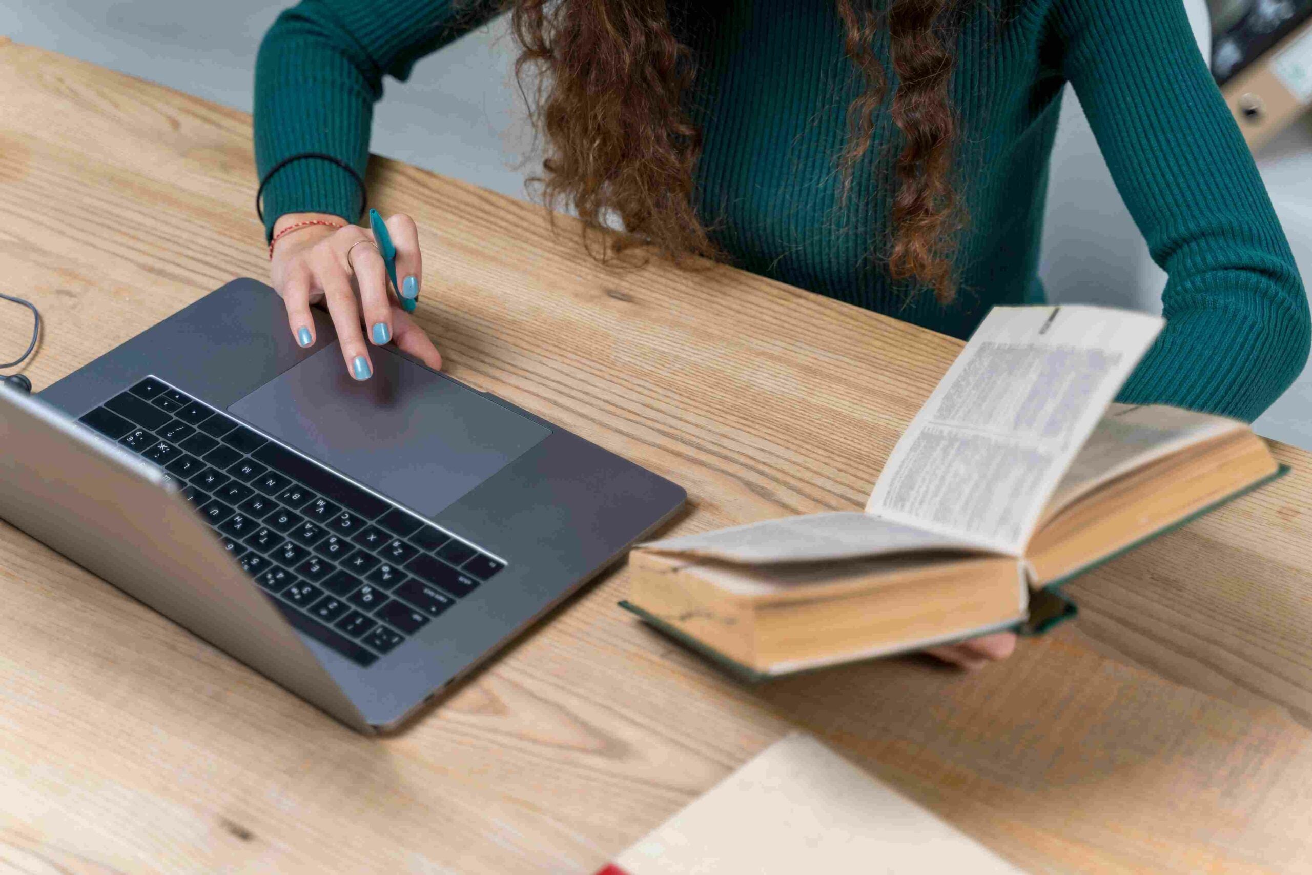 Uma mulher usa seu laptop enquanto segura um livro.