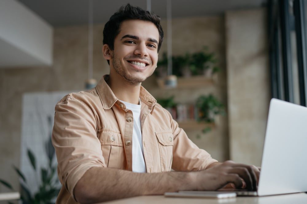 Man sitting at desk with laptop. He is smiling and focused on his work.