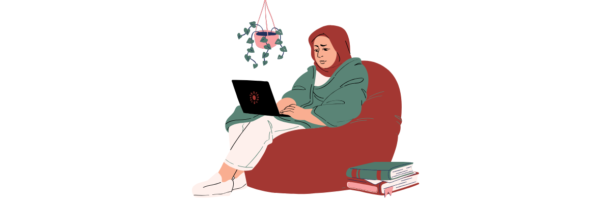 A woman wearing a hijab sits on a red bean bag chair with a laptop on her lap. She appears to be studying or working.