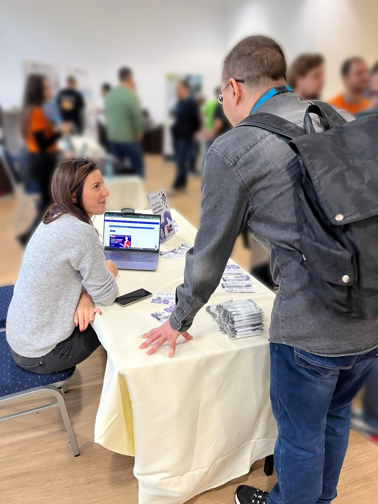 A man looking at a table with a woman and a laptop. The woman is sitting down.